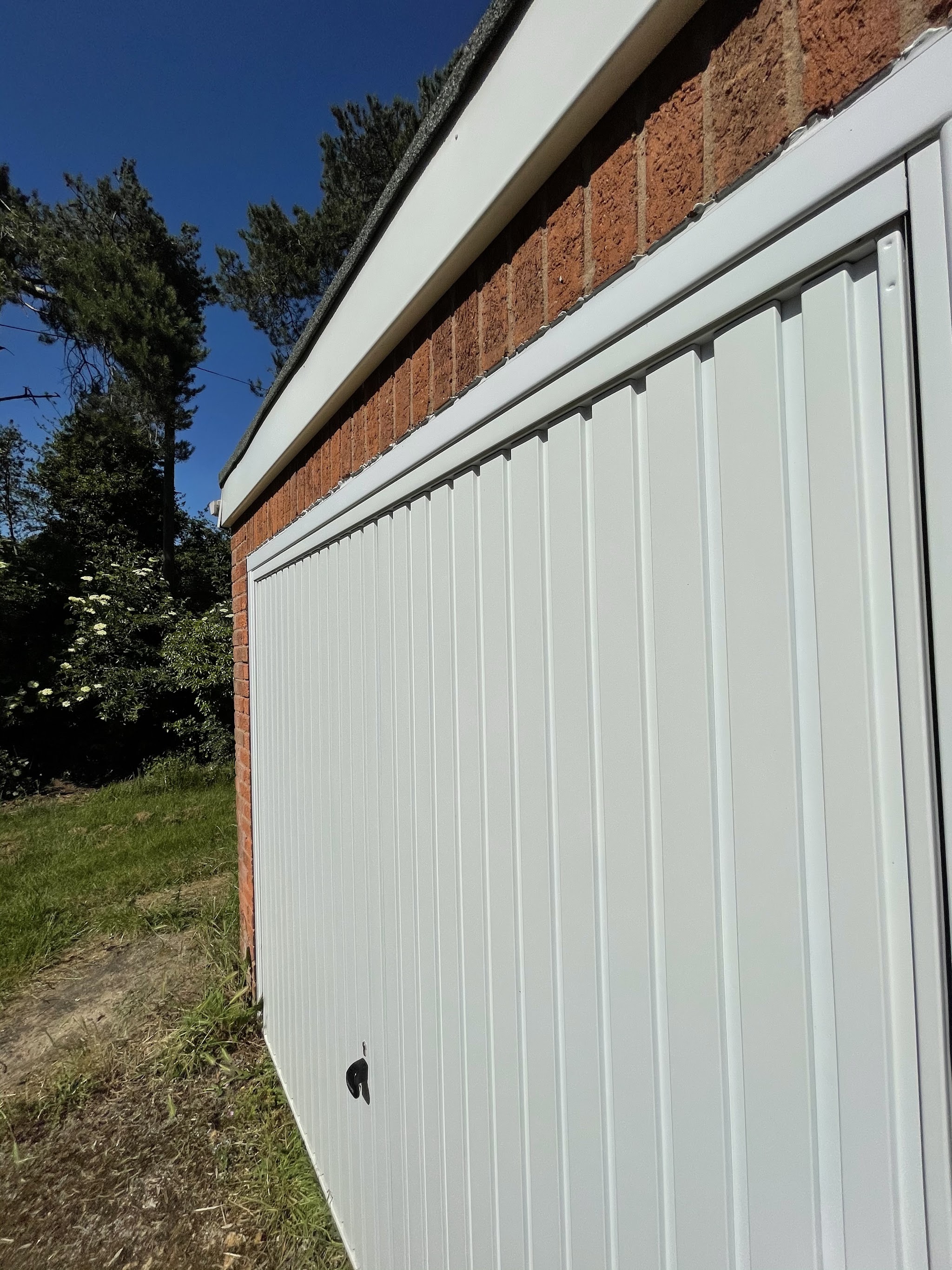 A freshly cleaned white garage door and fascia along a brick wall