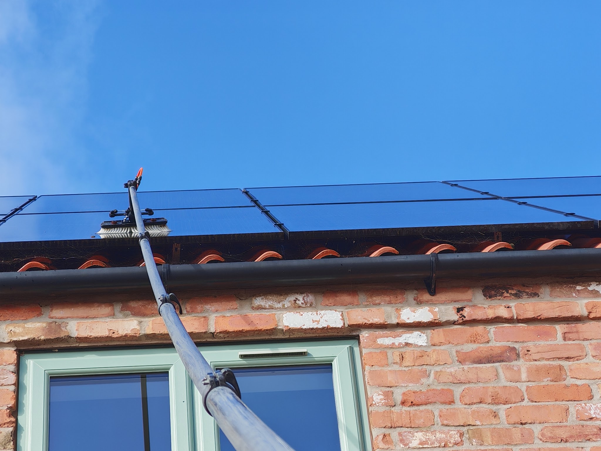 Solar panels above a sage green window being cleaned from the ground