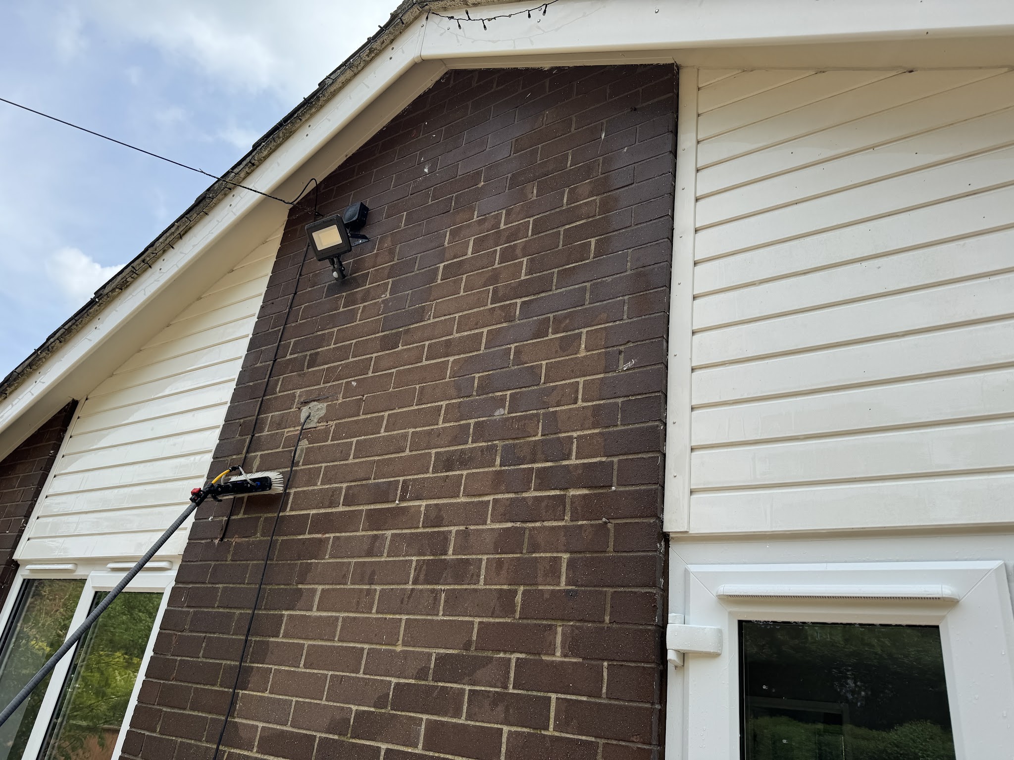A pole cleaning the walls and windows of a dark brick and white weatherboard house