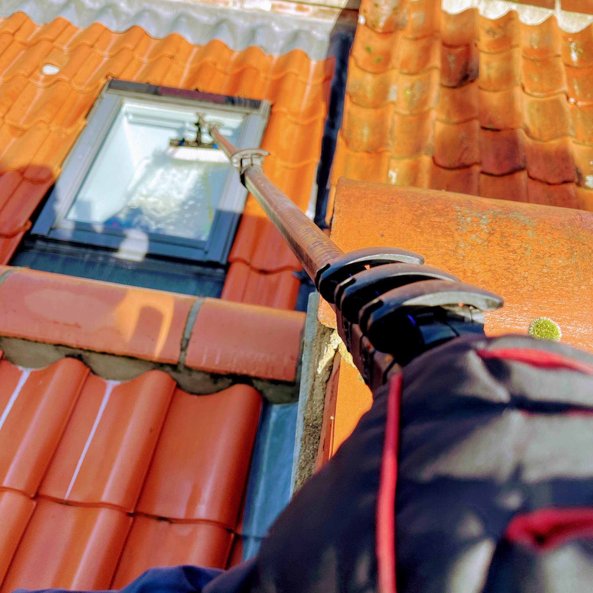 A pole brush guided onto a roof skylight set in orange pantiles