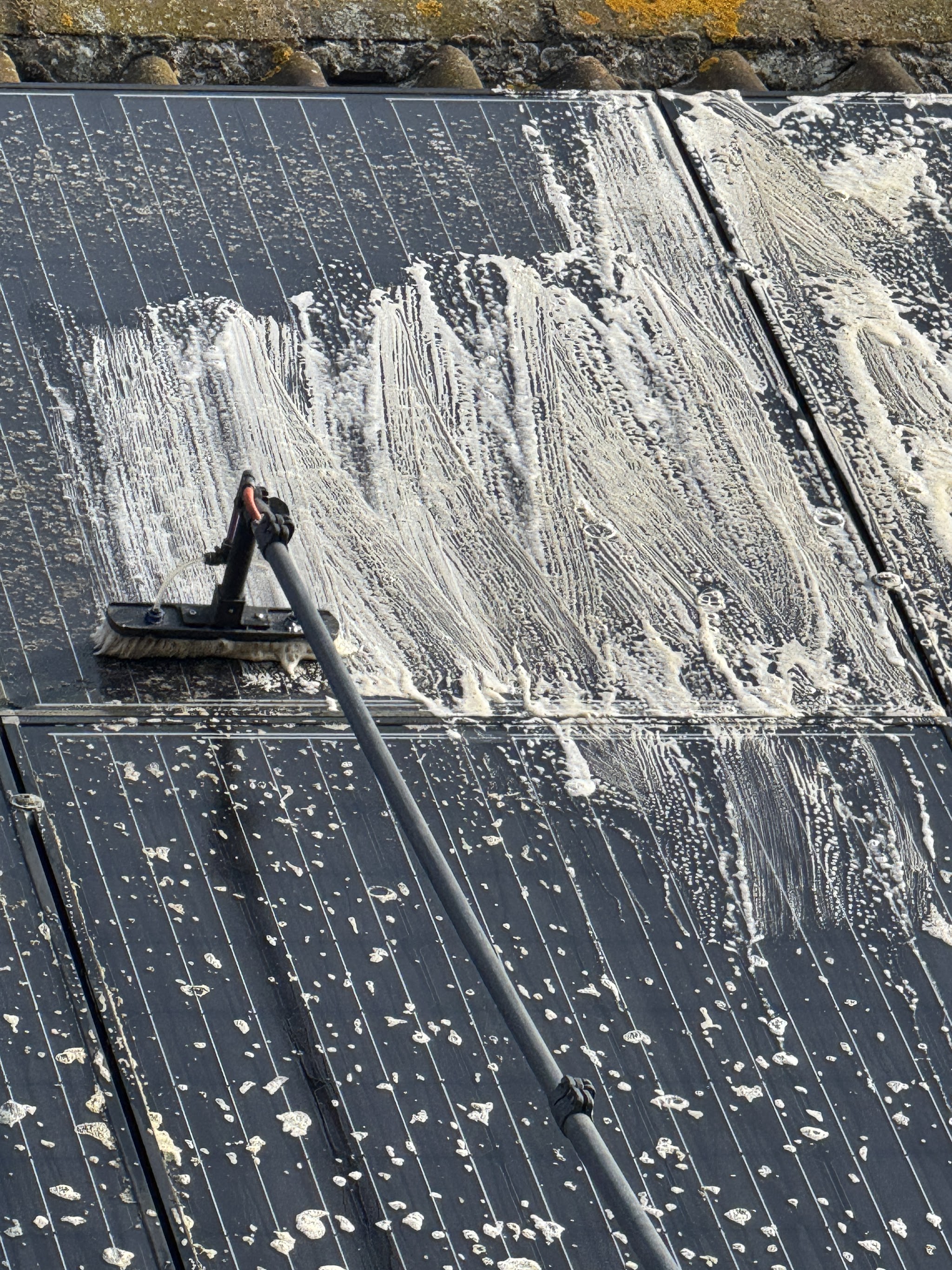Dirty solar panels part way through a wash, with the brush leaving clean strokes