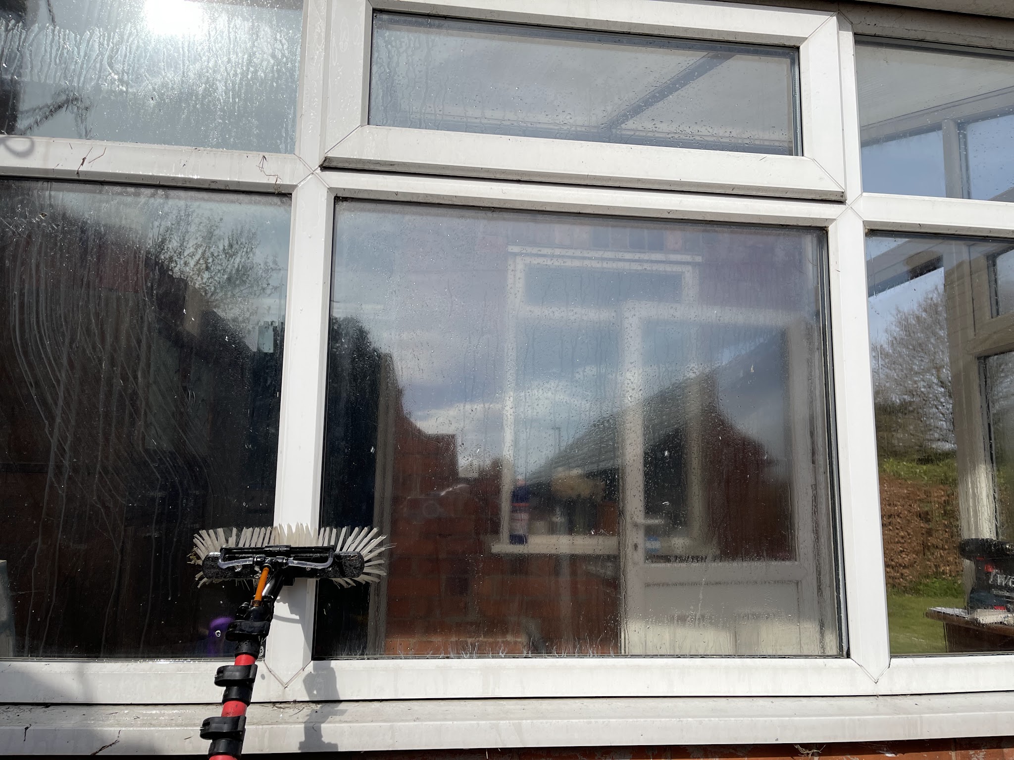 A brush head cleaning a white uPVC conservatory window