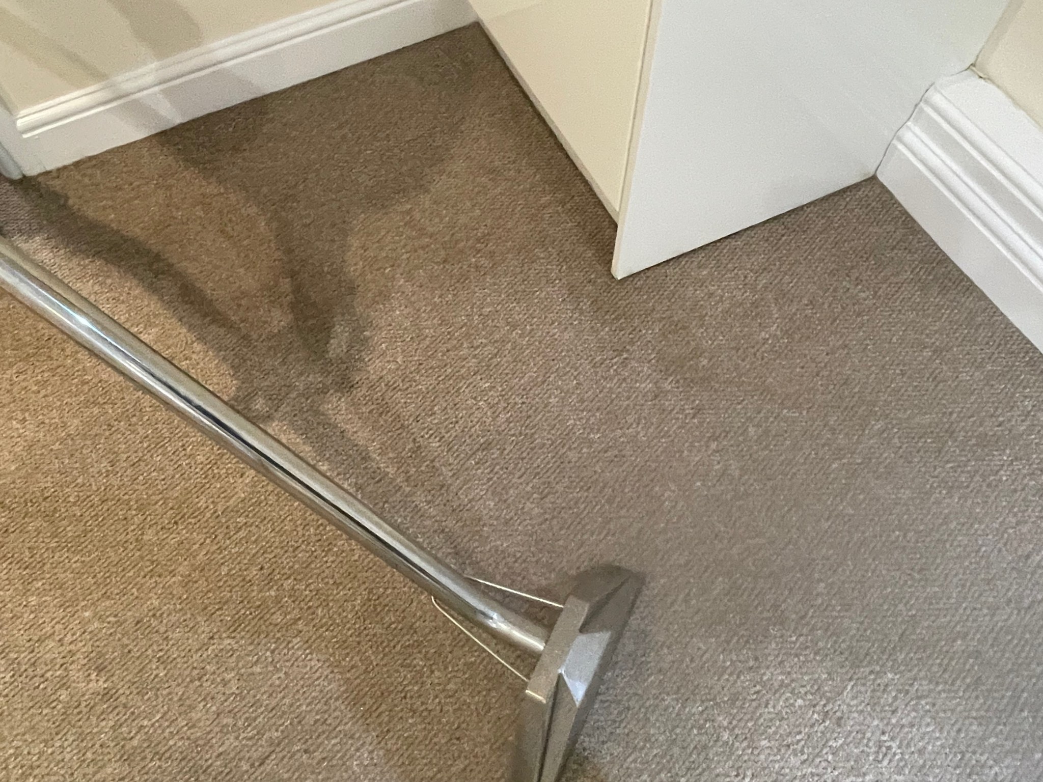 A carpet cleaning wand working into the corner of a bedroom carpet